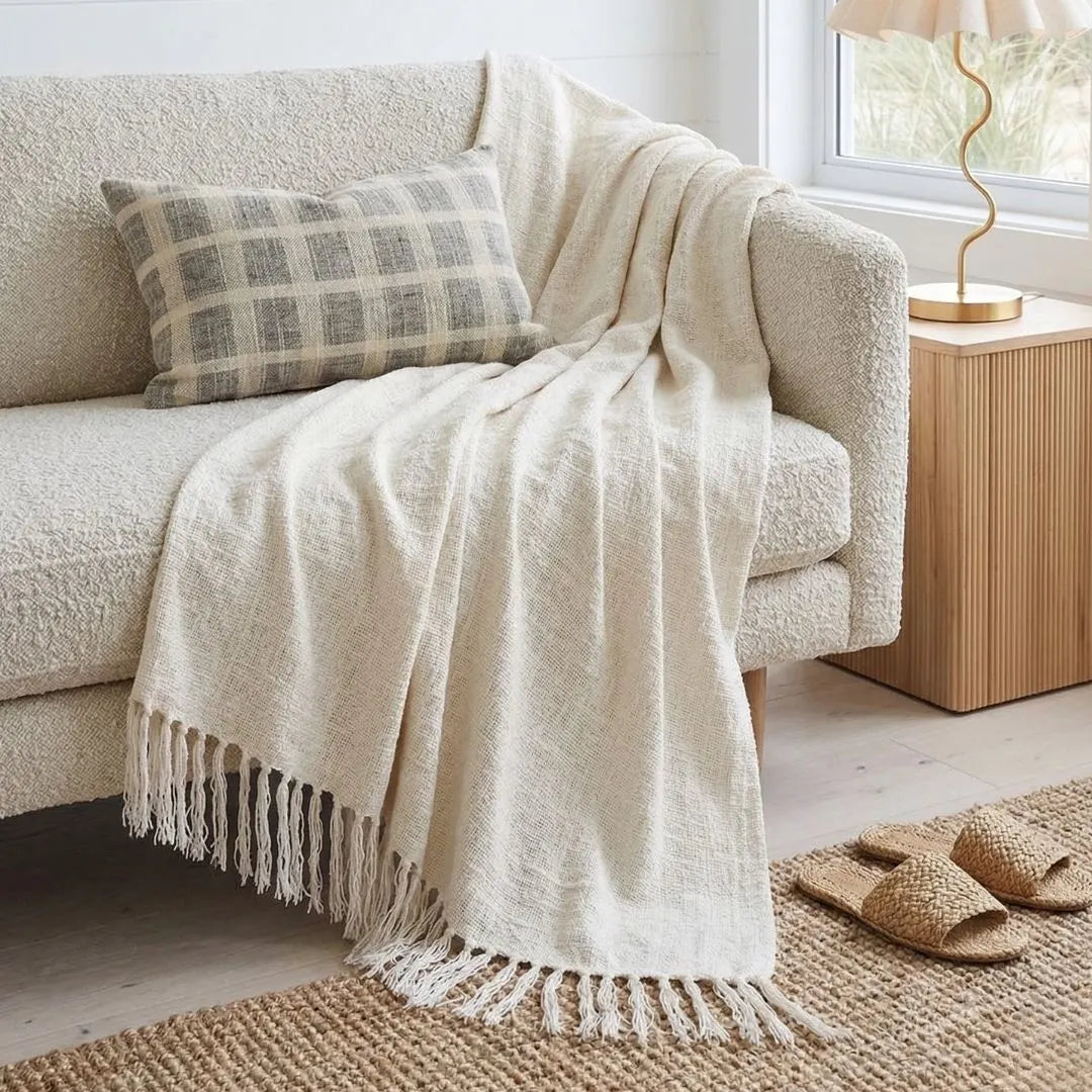 Beige blanket draped over a sofa with a plaid pillow in a cozy living room.