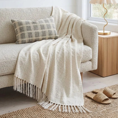 Beige blanket draped over a sofa with a plaid pillow in a cozy living room.