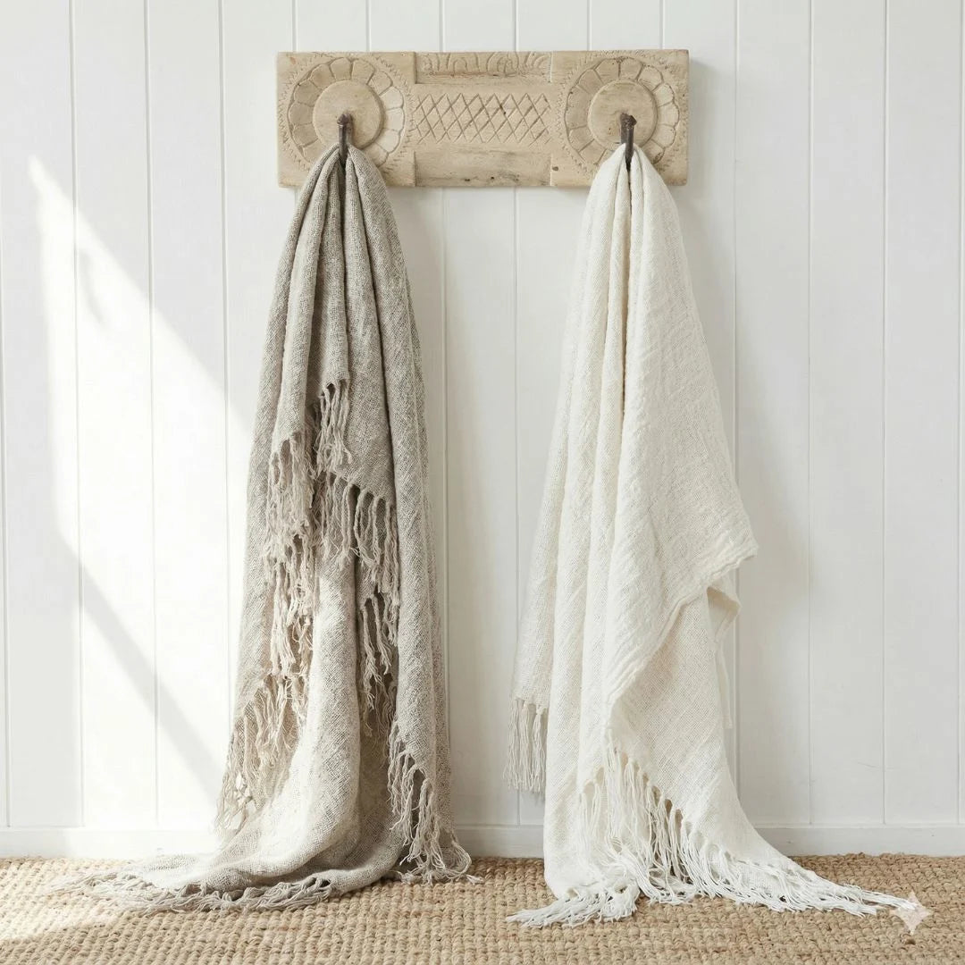 Two textured linen throw blankets hanging on a decorative wooden hook against a white paneled wall.