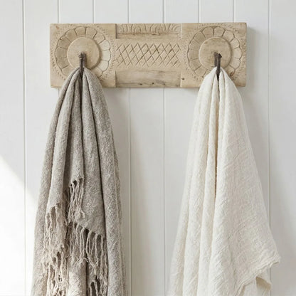 Two textured linen throw blankets hanging on a decorative wooden hook against a white paneled wall.