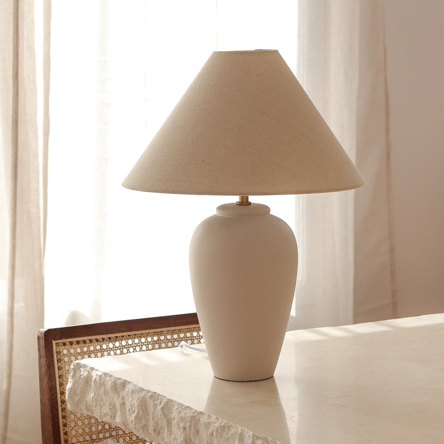 Beige table lamp on a surface with light curtains in the background