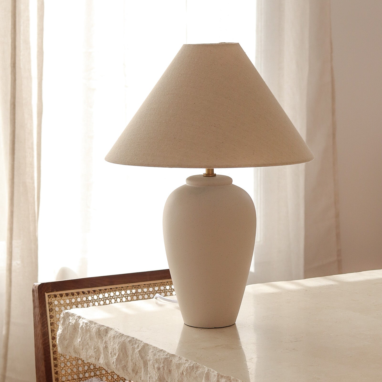 Beige table lamp on a surface with light curtains in the background