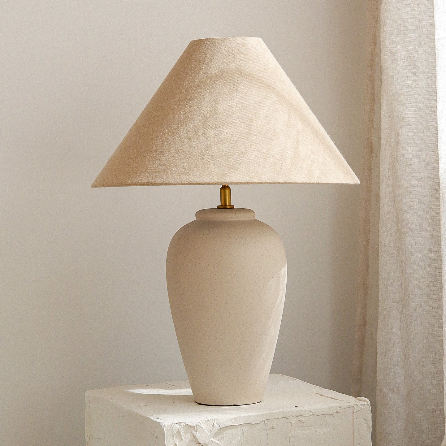 Beige table lamp with a textured shade on a marble surface against a neutral wall.