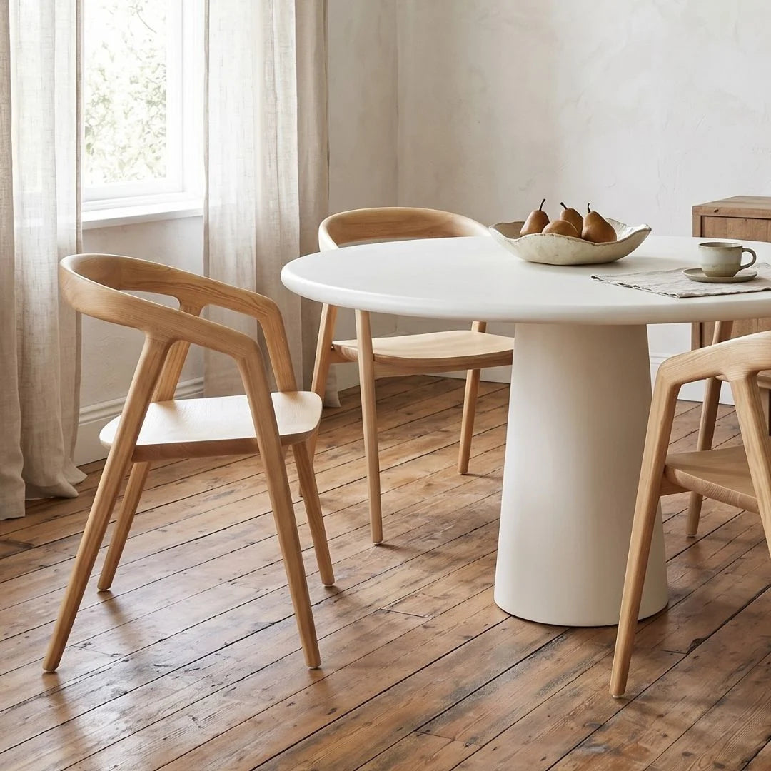 Dining area with a white round table and wooden chairs on a wooden floor.