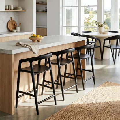 Modern kitchen with wooden island and black bar stools, large windows allowing natural light.