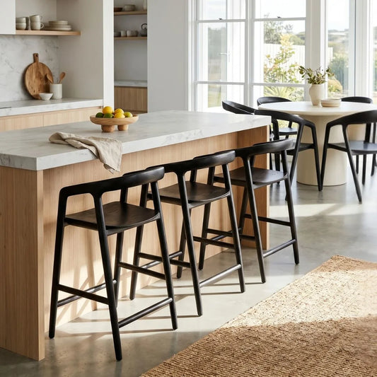 Modern kitchen with wooden island and black bar stools, large windows allowing natural light.
