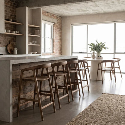 Modern kitchen with marble island and wooden stools, large windows allowing natural light.