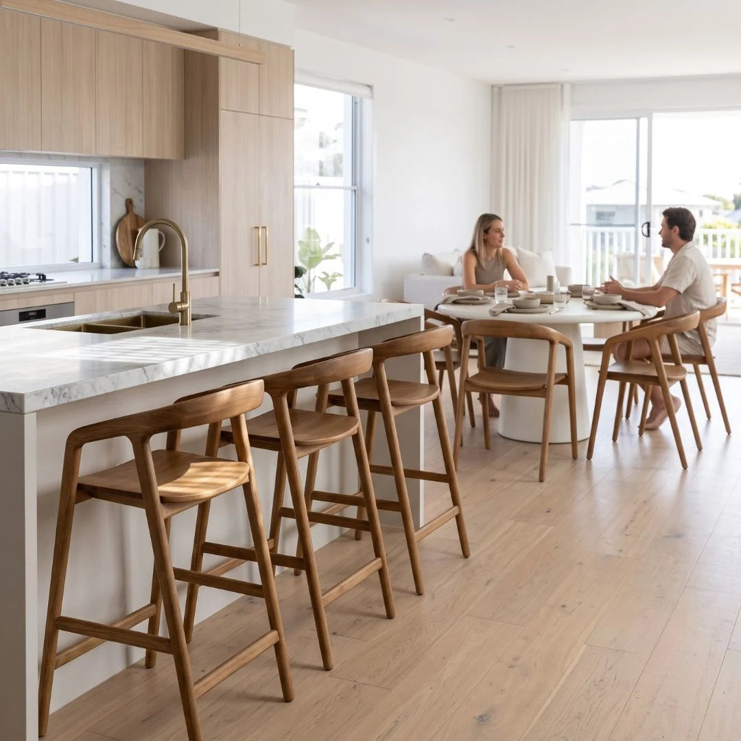 A modern kitchen island with a white marble countertop and four wooden bar stools in a bright, contemporary dining area where a couple is seated at a round table.