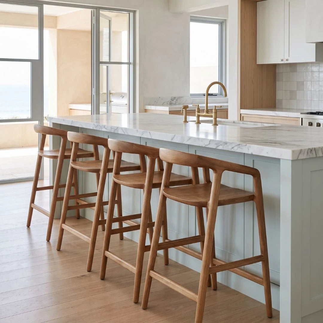 A modern kitchen island with a white marble countertop and four wooden bar stools, set in a bright, contemporary kitchen with light wood floors and white cabinetry.