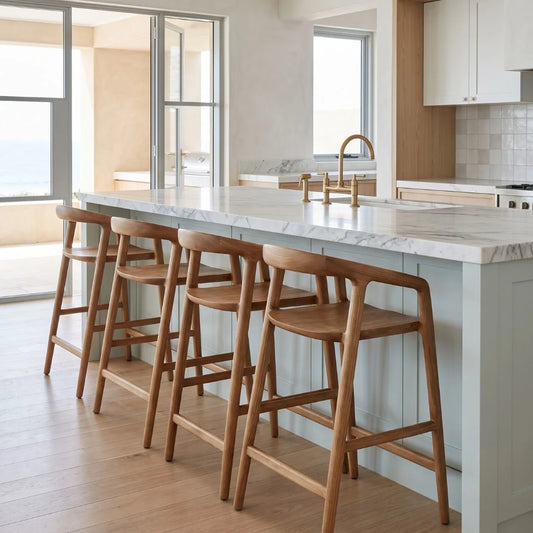 A modern kitchen island with a white marble countertop and four wooden bar stools, set in a bright, contemporary kitchen with light wood floors and white cabinetry.