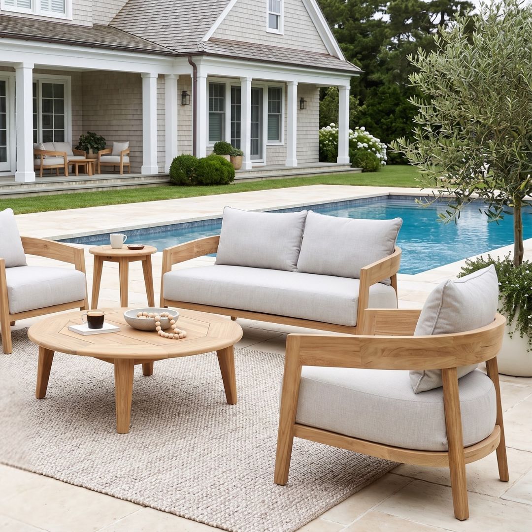 Outdoor patio set with wooden furniture and white cushions by a poolside.