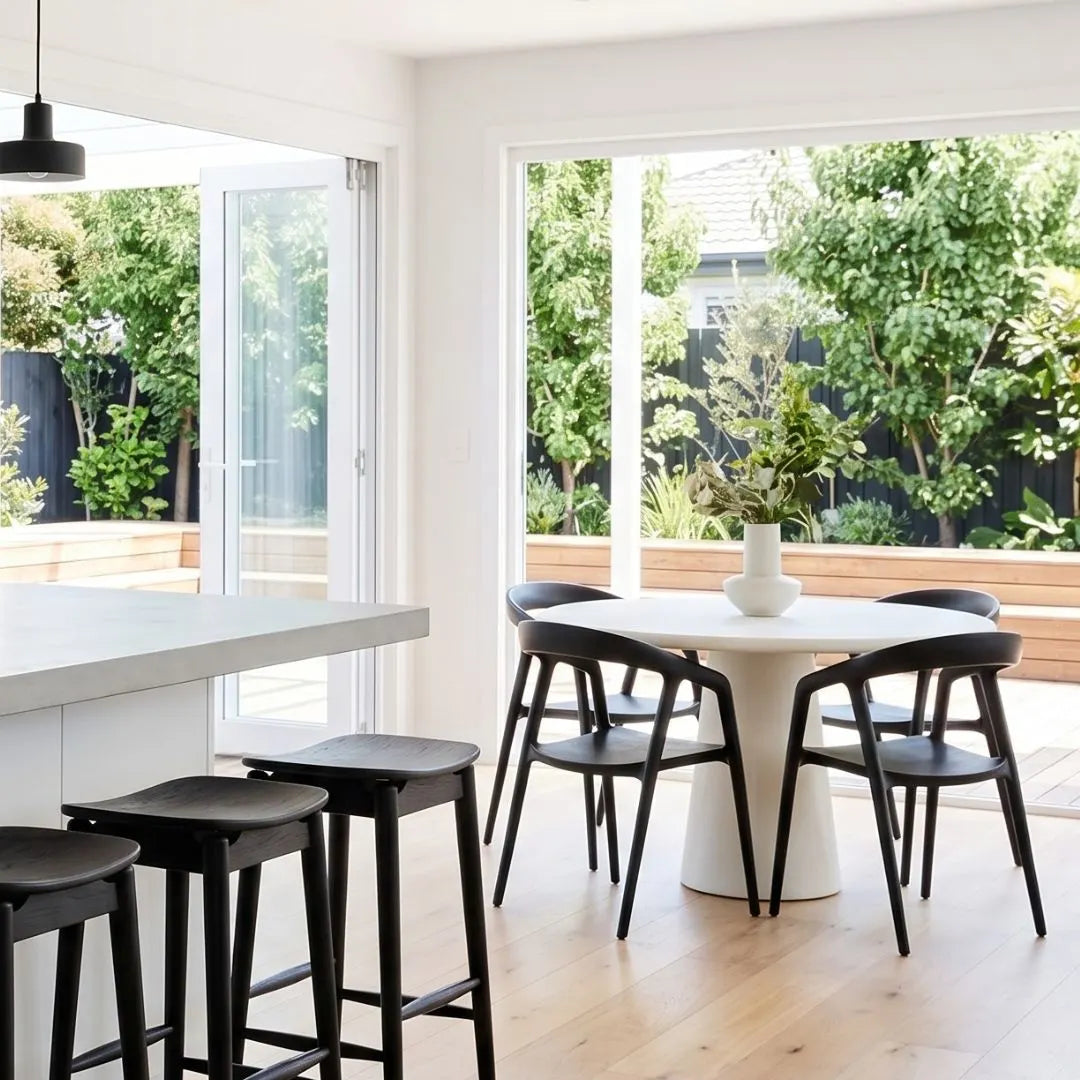 Modern kitchen with white island, round table, and black chairs.