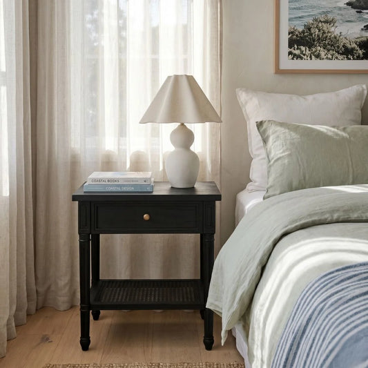 Bedroom with a nightstand, lamp, and books near a bed with white and green bedding.