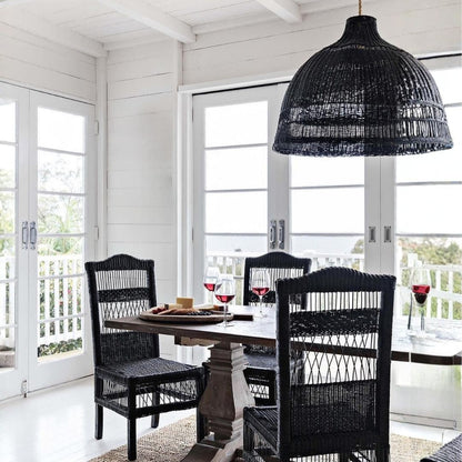 Dining area with black wicker chairs and table under a black woven pendant light.