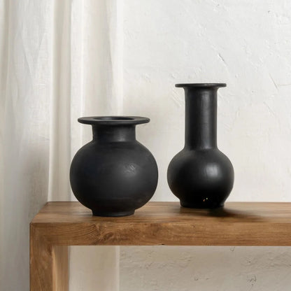 Two black ceramic vessels on a wooden surface with a white background by Sun Republic