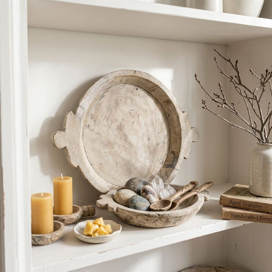 Decorative shelf with wooden platter, candles, stones, and a vase with branches.