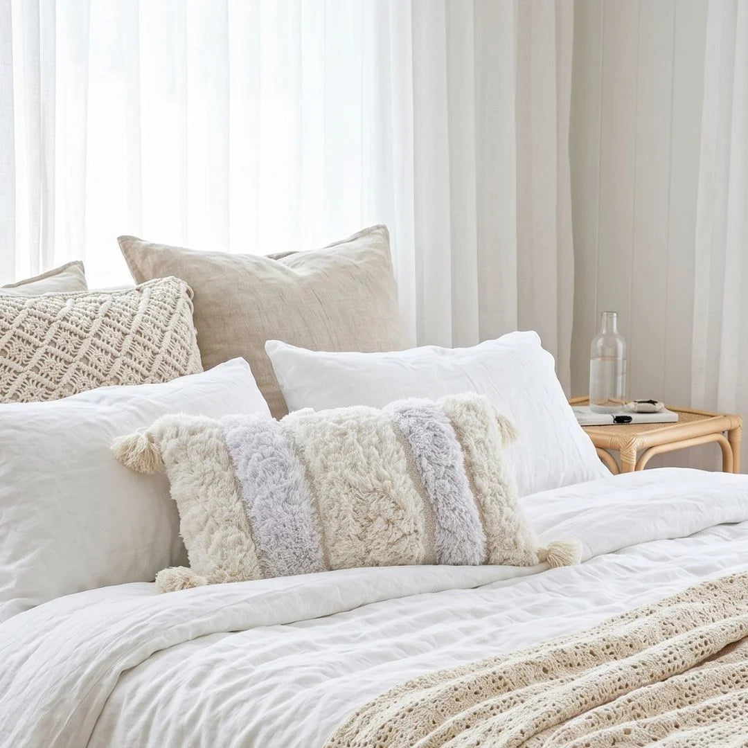 Neatly made bed with decorative pillows and a side table in a bedroom setting.