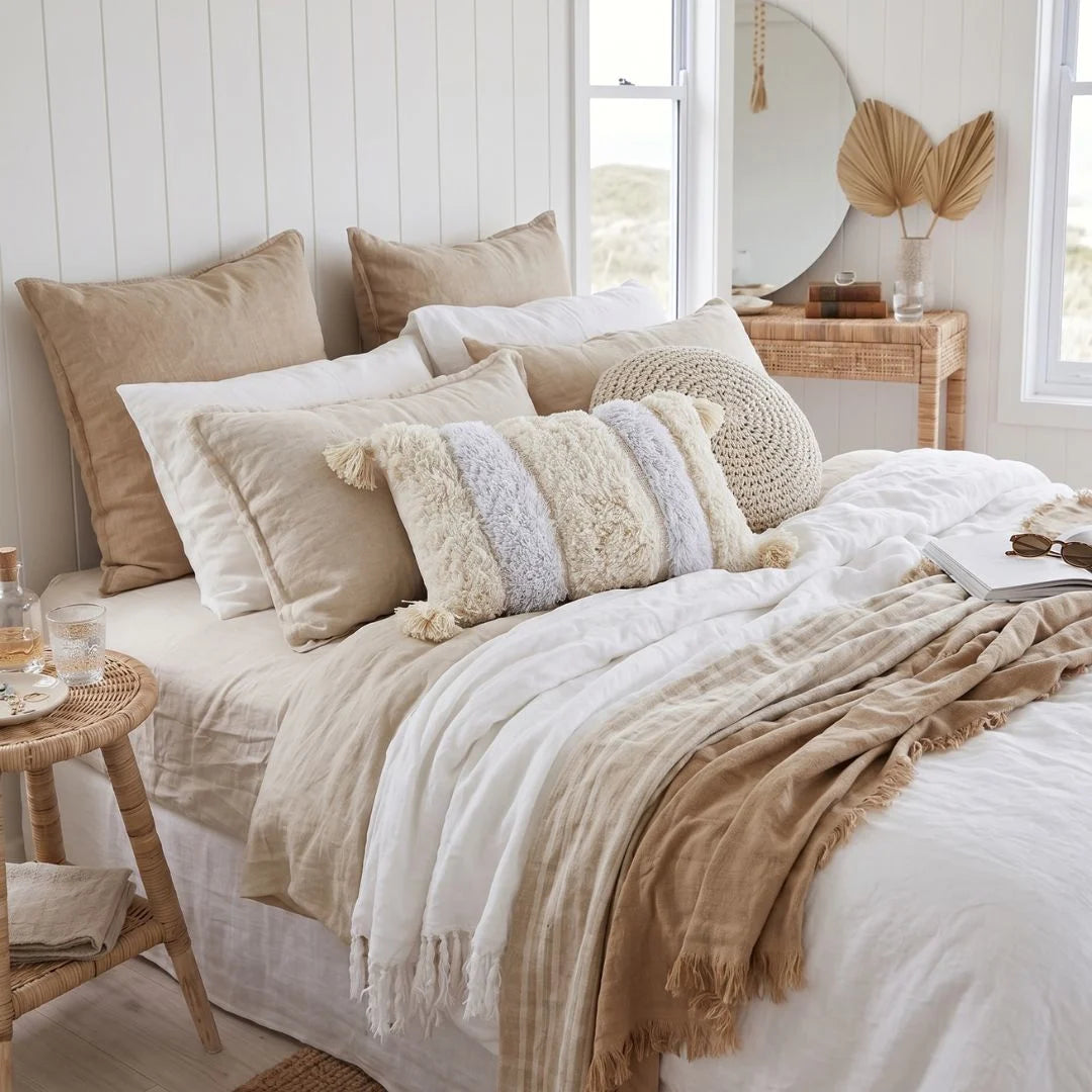 Neatly made bed with decorative pillows and a blanket in a bright bedroom.