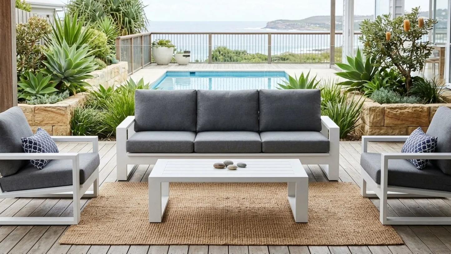 Outdoor patio set with gray cushions and a white coffee table in a garden setting.