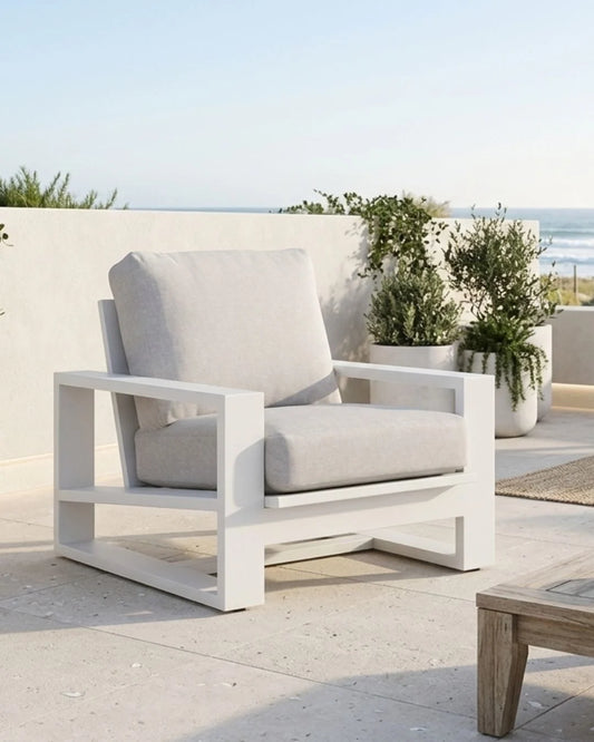 White outdoor chair with gray cushions on a patio with plants and ocean view