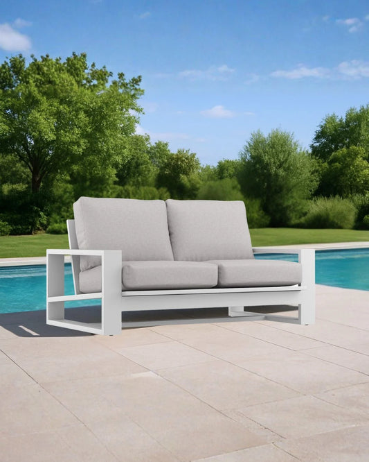 Gray outdoor sofa with white frame near a pool with greenery in the background