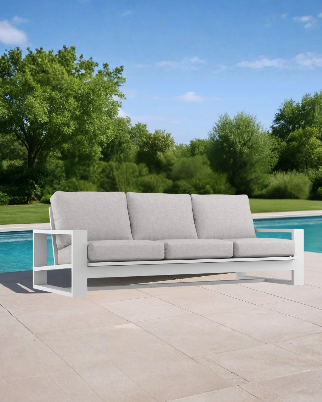 Gray outdoor sofa with white frame on a patio near a pool with trees in the background