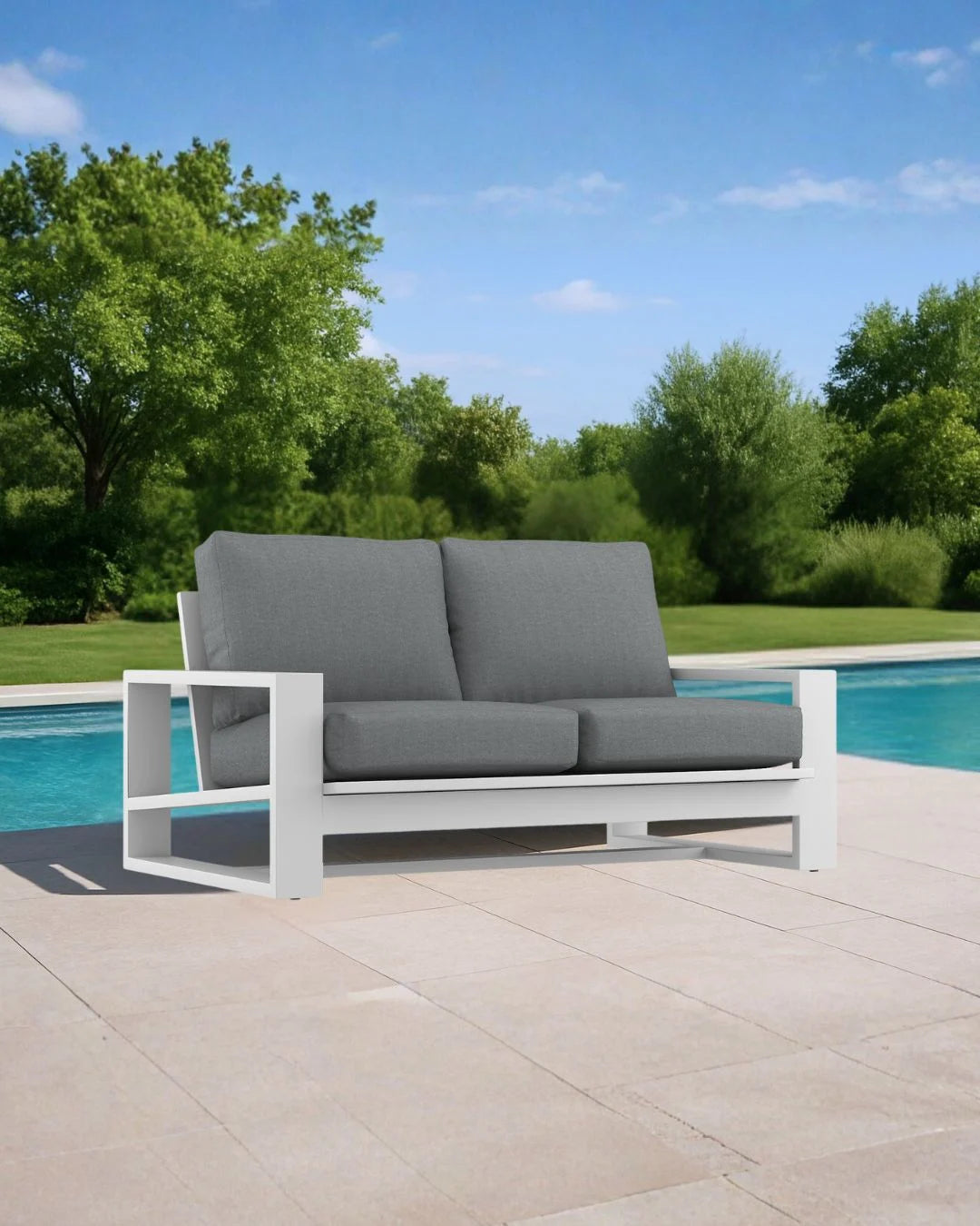 Gray outdoor sofa with white frame near a pool with green trees in the background