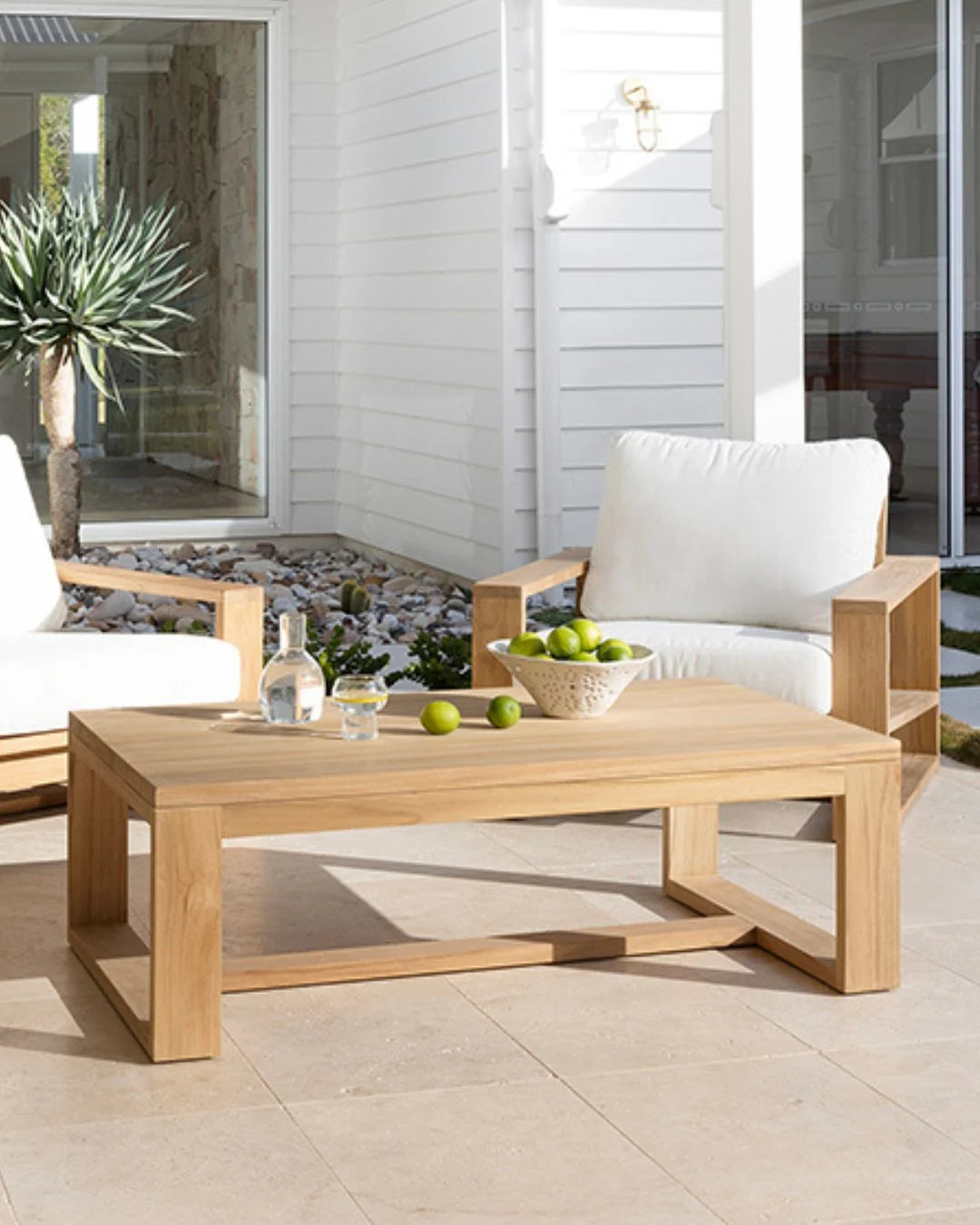 Outdoor patio setting with wooden coffee table, chairs, and decorative items.