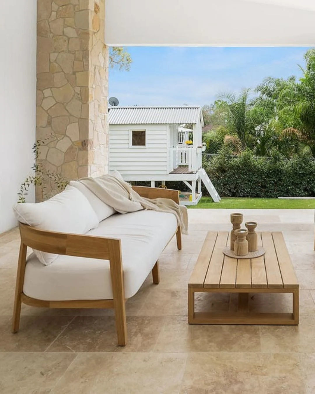 Outdoor patio with wooden sofa, coffee table, and view of a white house and garden.