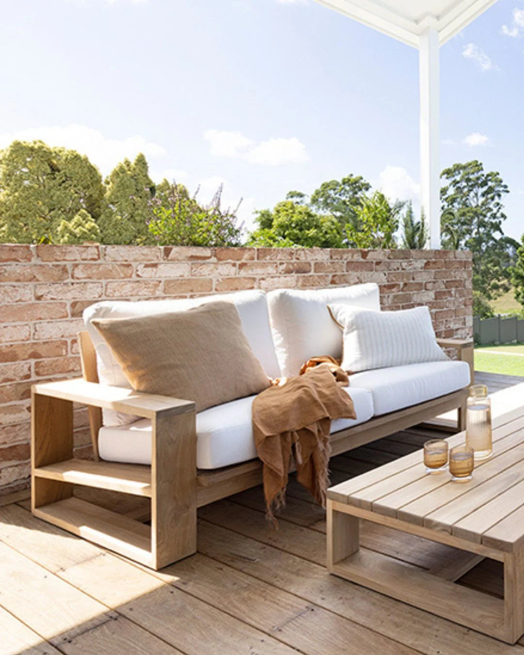Outdoor patio with wooden furniture, cushions, and a brick wall.