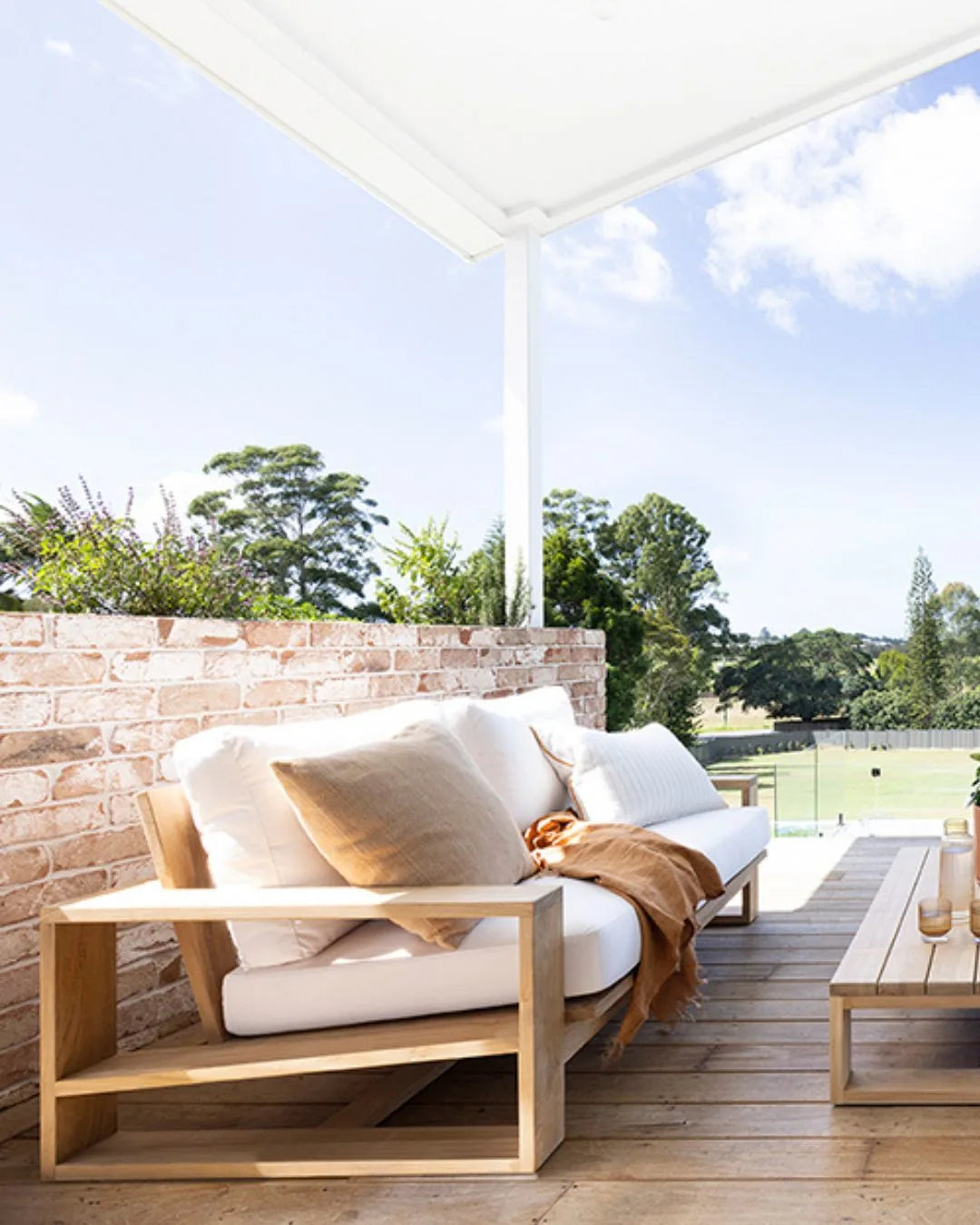 Outdoor seating area with a wooden bench and white cushions under a white canopy.