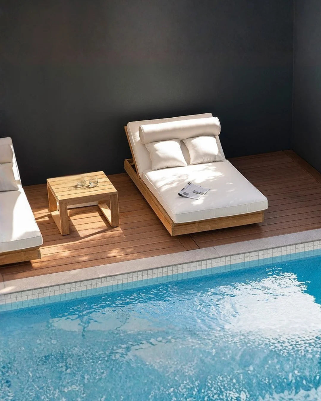 Modern outdoor lounge chair with white cushions by a poolside.