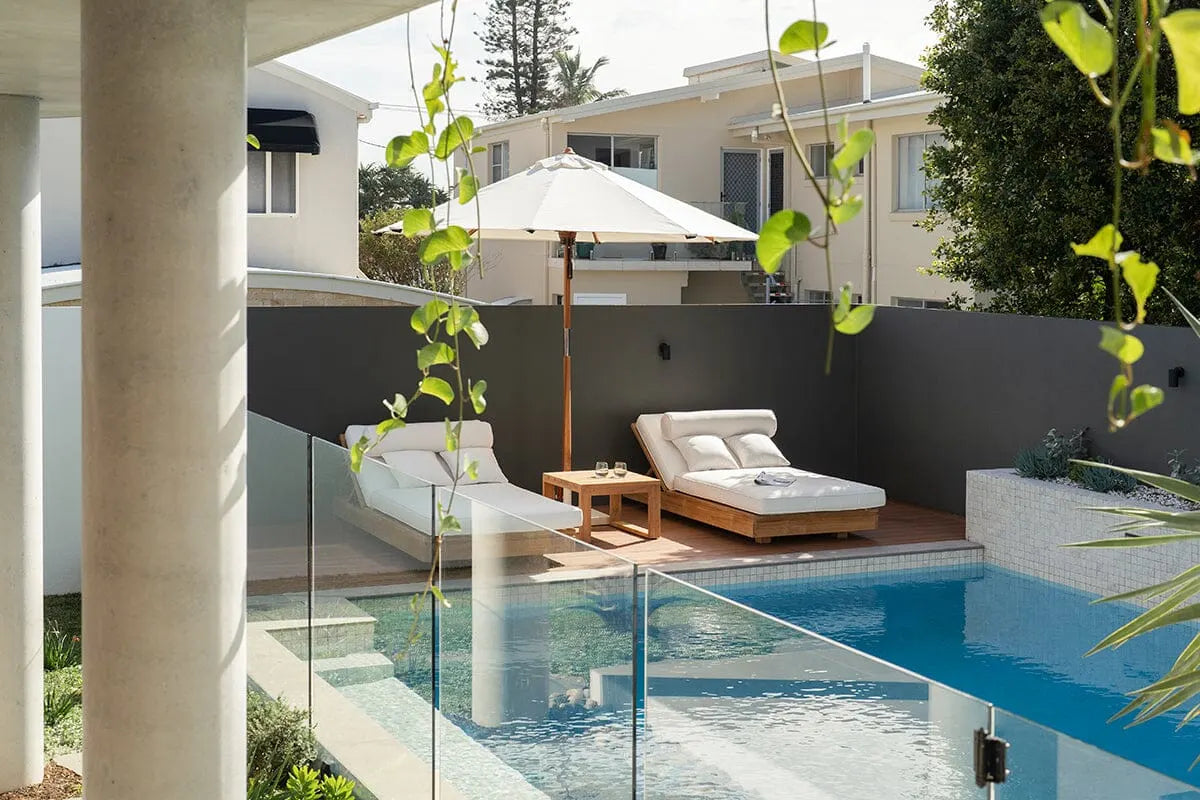 Outdoor pool area with lounge chairs, umbrella, and modern house in the background
