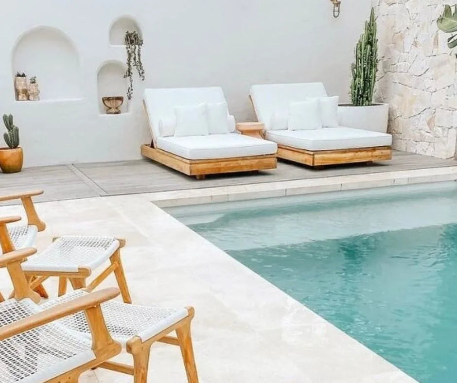 Outdoor seating area with wooden chairs and white cushions by a pool.