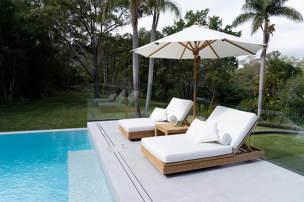 Outdoor lounge chairs with a large umbrella by a poolside in a garden setting