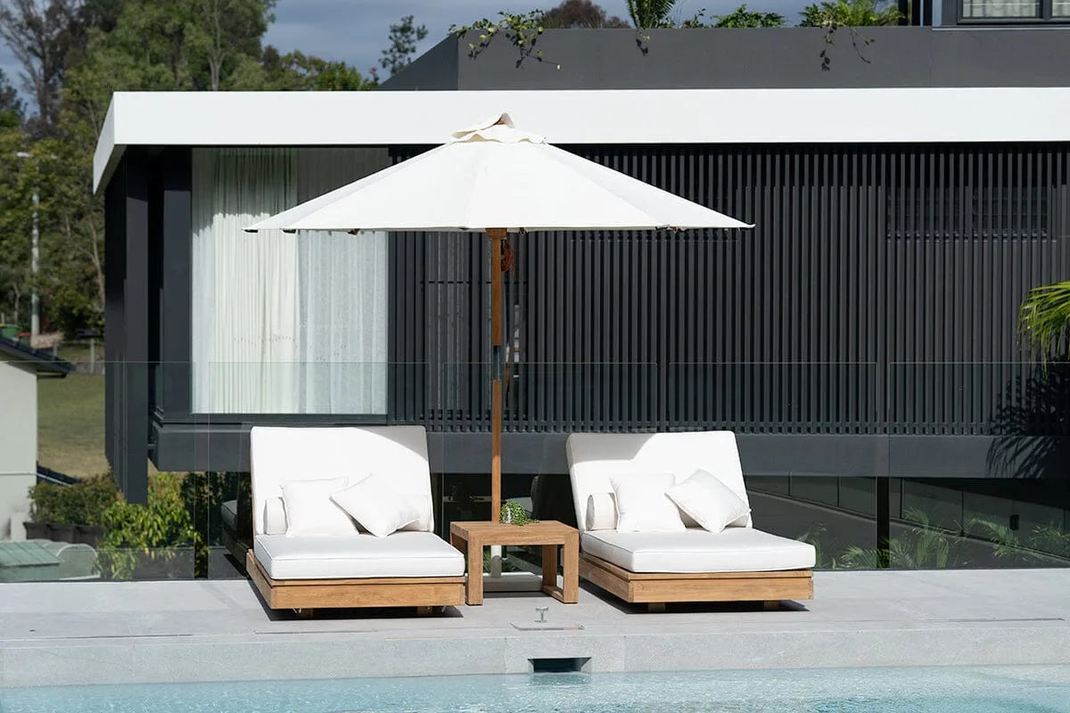 Two white lounge chairs with cushions and a matching umbrella by a poolside.