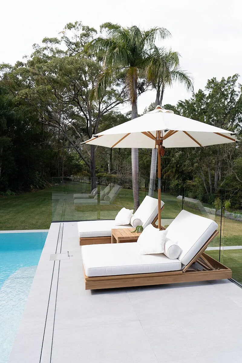Modern outdoor lounge set with white cushions and a large umbrella by a pool.