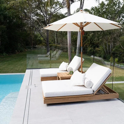 Modern outdoor lounge set with white cushions and a large umbrella by a pool.