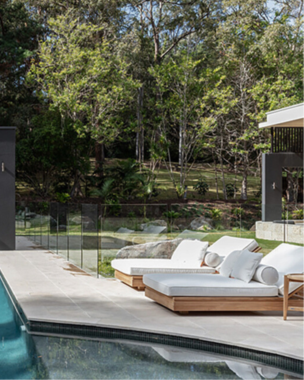 Modern outdoor lounge area with white outdoor sunlounge and a pool in a forested setting