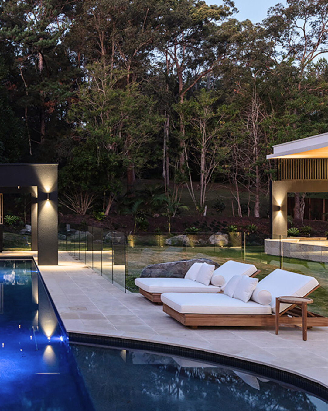 Modern outdoor sunlounge area by a pool with trees in the background
