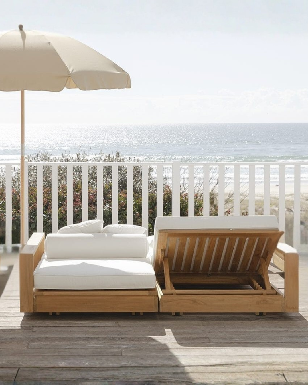 Teak outdoor double sunlounge with white cushions on a deck overlooking the ocean.