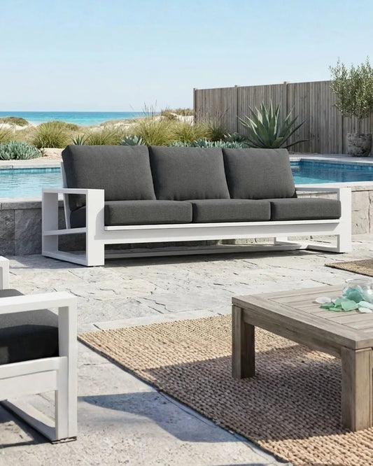 Outdoor patio set with gray sofa, wooden table, and pool in the background