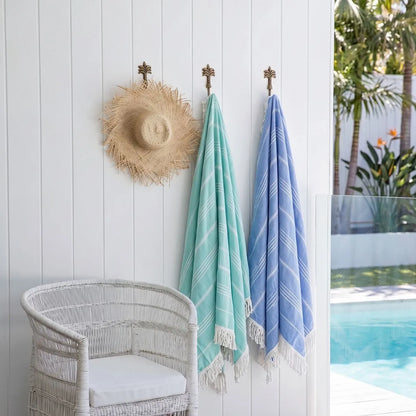Towels hanging on a hook next to a poolside chair with a hat and view of a pool.