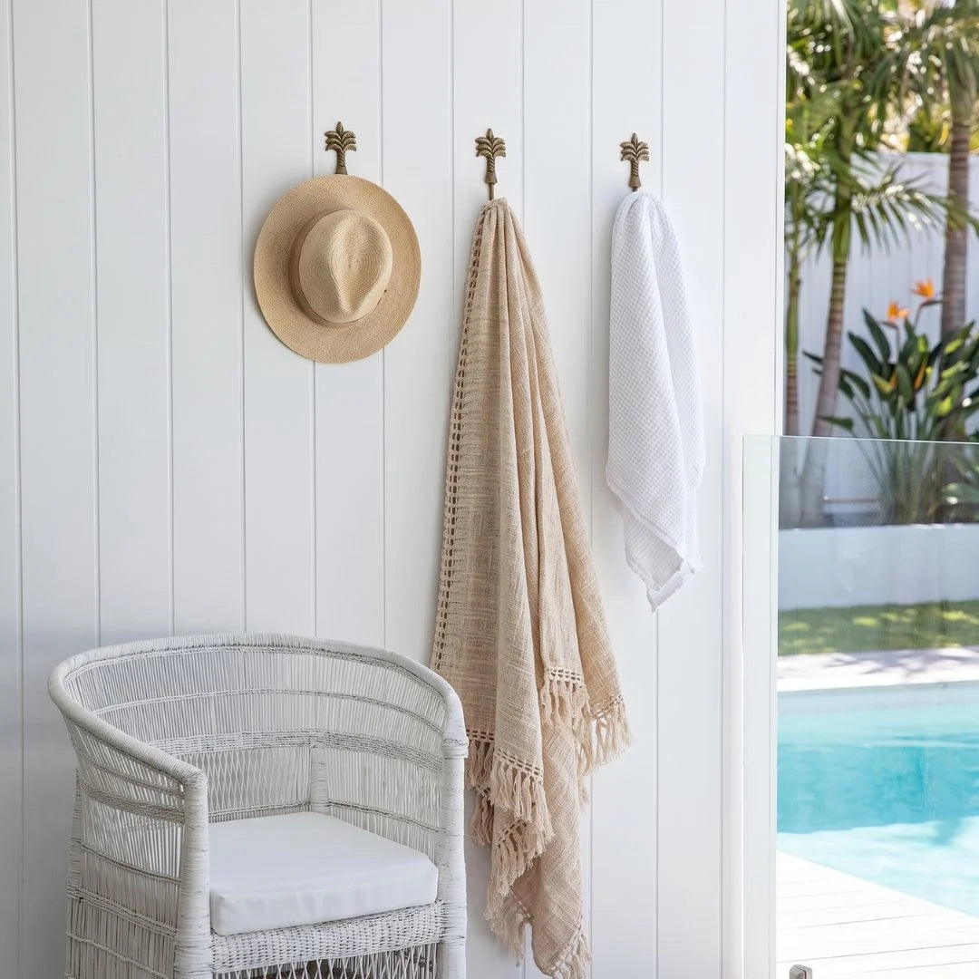 Wicker chair with white cushion, hat, and towel hanging on a white wall by a poolside.