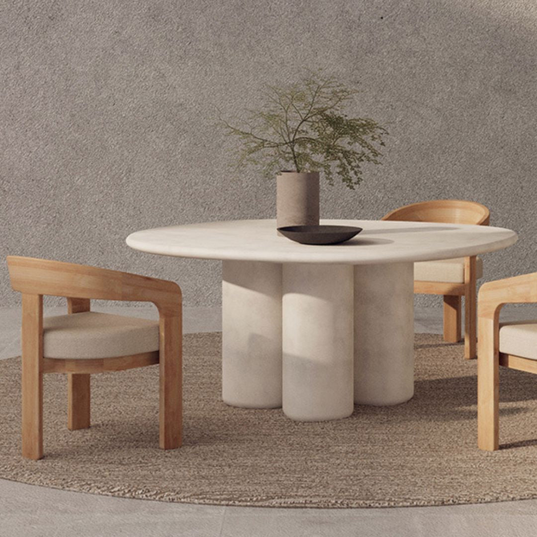 Organic Round stone dining table with wooden chairs against a textured wall.