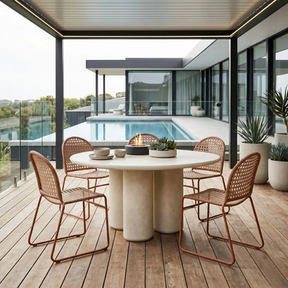 Outdoor dining area with a round table and chairs on a wooden deck, pool in the background.