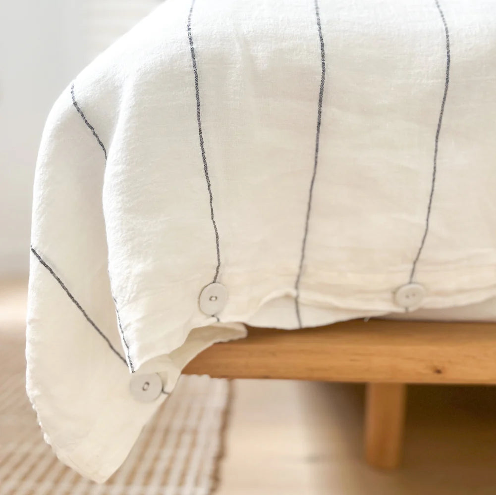 Close-up of a white quilt with black stitching on a wooden bed frame.