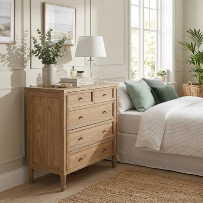 Wooden dresser in a bedroom with a bed, lamp, and plants.