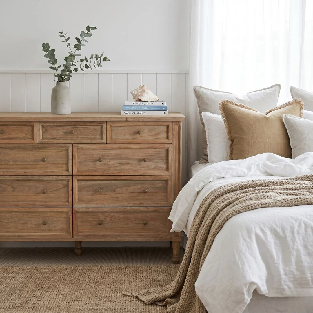 Wooden dresser next to a bed with pillows and a blanket in a bedroom setting.