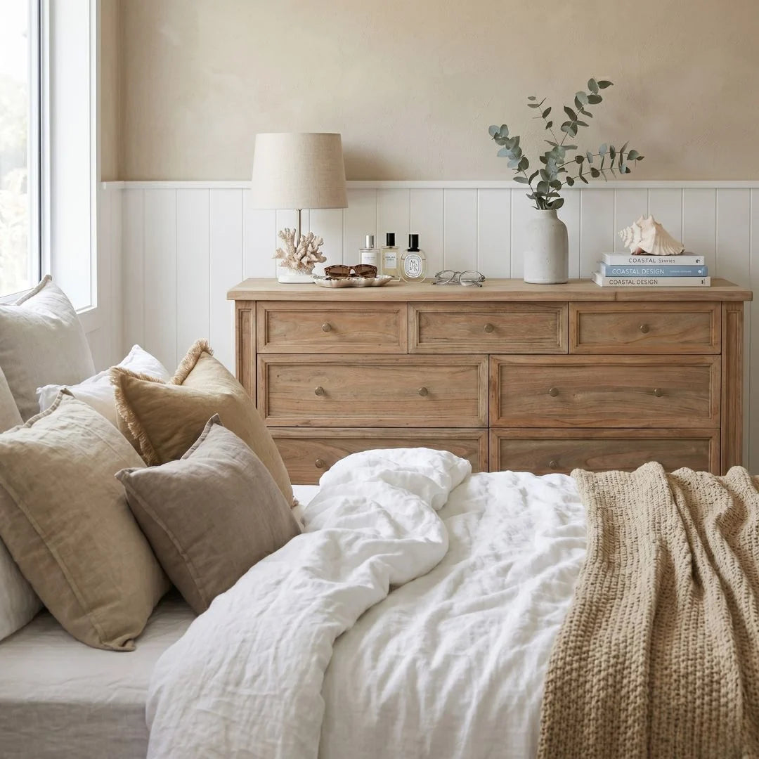 Bedroom with wooden dresser, white bedding, and decorative items.